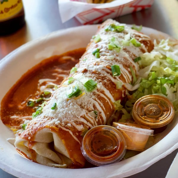A large, saucy burrito from Rollies Mexican Patio, topped with cheese, sour cream, and green onions.