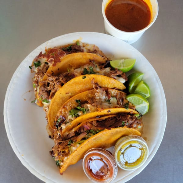 Rollies Mexican Patio's birria tacos with lime wedges, consommé, and two small sauce cups.