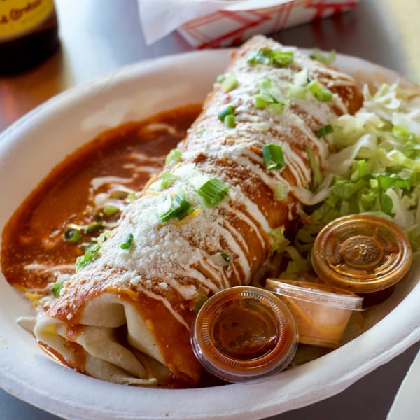 A large, saucy burrito topped with cheese, sour cream, and green onions, served with shredded lettuce and sauces.