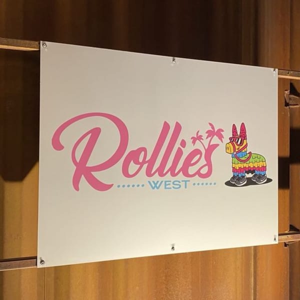 Rollies Mexican Patio sign with pink text, palm trees, and a colorful piñata wearing sunglasses and sneakers.