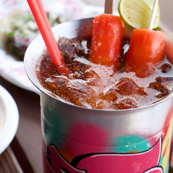 Close-up of a colorful Mexican drink with ice, a red straw, watermelon chunks, and a lime.