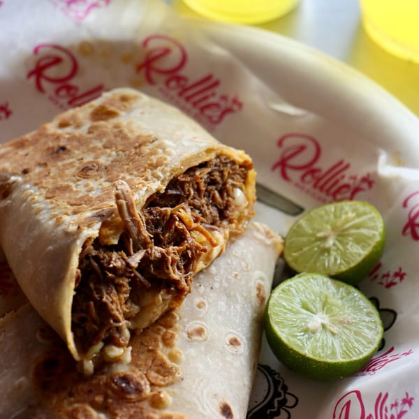 Rollies Mexican Patio's shredded beef burrito, cut open, with two lime halves on branded paper.