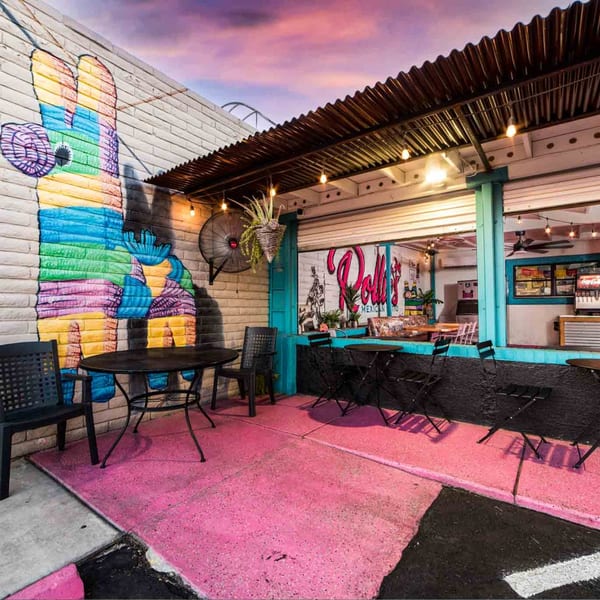 Pink patio with black tables and chairs outside a restaurant with a colorful piñata mural.